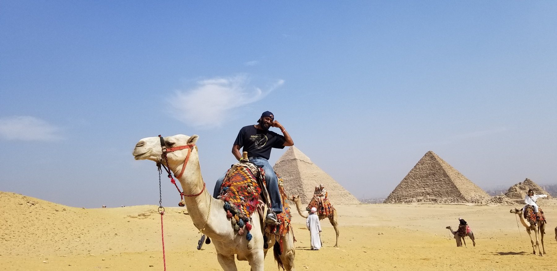 Darnell riding a camel with the Pyramids of Giza behind him