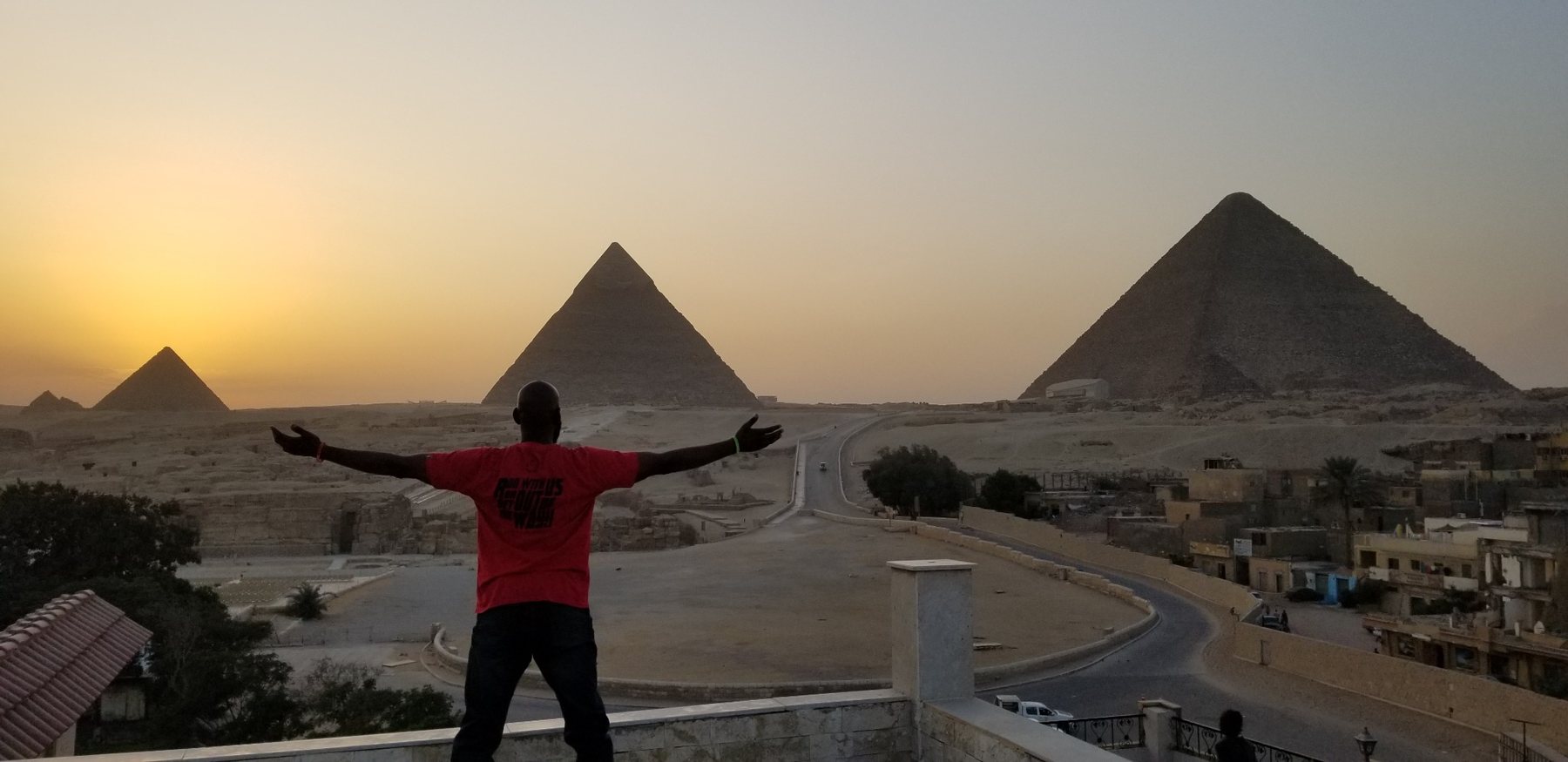 Darnell standing with arms open toward the pyramids at sunset